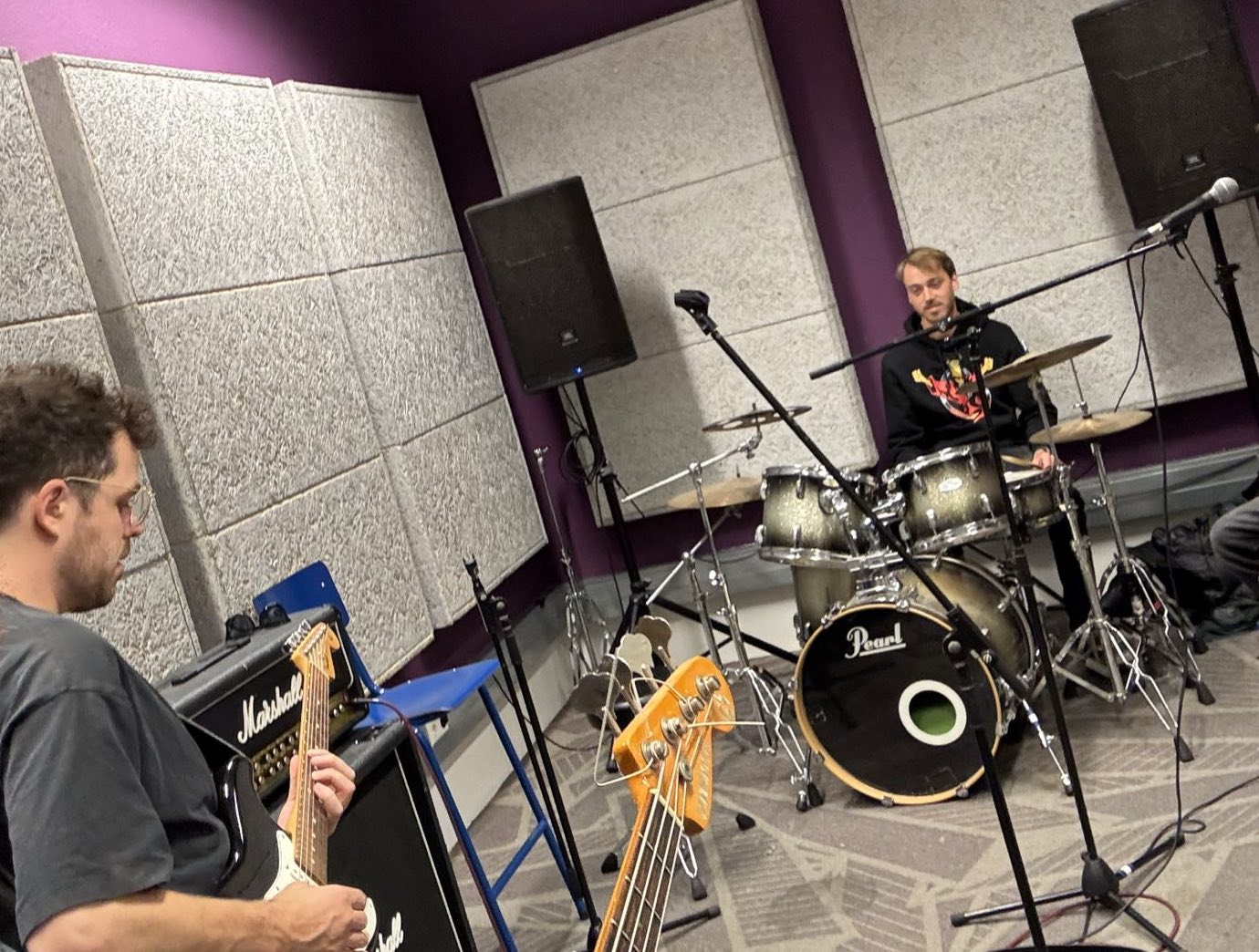 Band repeteert in een oefenruimte: gitarist en bassist voor een Marshall-versterker, drummer achter het drumstel