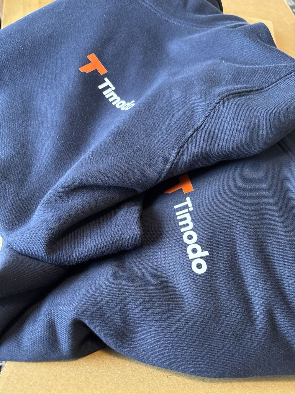 Twee donkerblauwe Timodo-truien met het oranje Timodo-logo